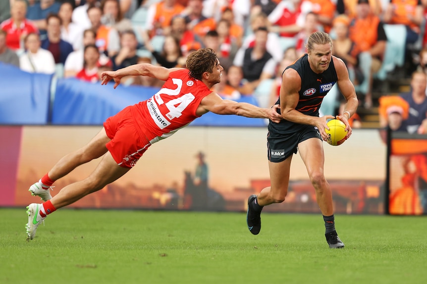 An AFL player looks ahead as he gets ready to kick the ball towards goal while a defender throws out an arm to stop him. 