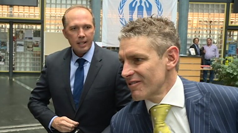 Mr Maclachlan shakes someone's hand, as Mr Dutton watches on while buttoning his jacket.