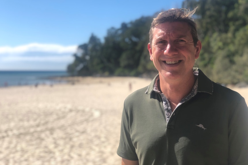 Graham Bradford stands outside on the beach at Noosa.