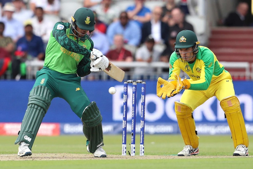 The ball is about to hit Quinton de Kock's bat as he plays a cross-bat shot. Alex Carey has his gloves in catching position.