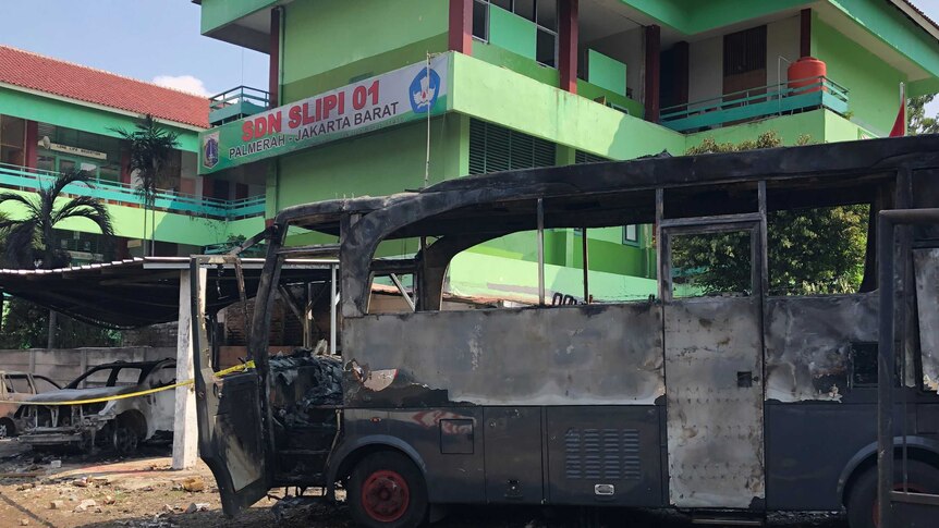 An burned Indonesian police bus sits in front of a green government building in Jakarta.