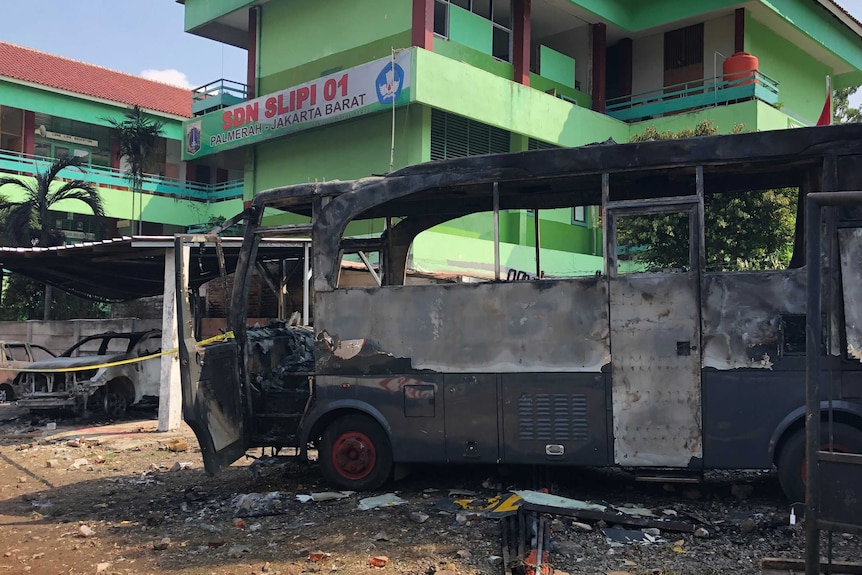 An burned Indonesian police bus sits in front of a green government building in Jakarta.