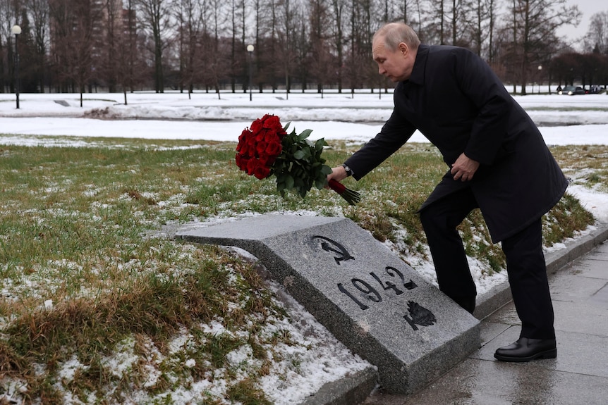 Putin leans to put roses on a grave in a cemetery.