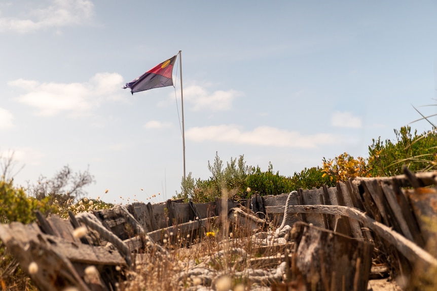 A hybrid of the Australian and Aboriginal flags at the beach, through the wreck of a weathered boat