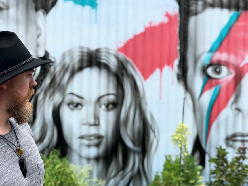 Man looking intently at a mural of musician's portraits