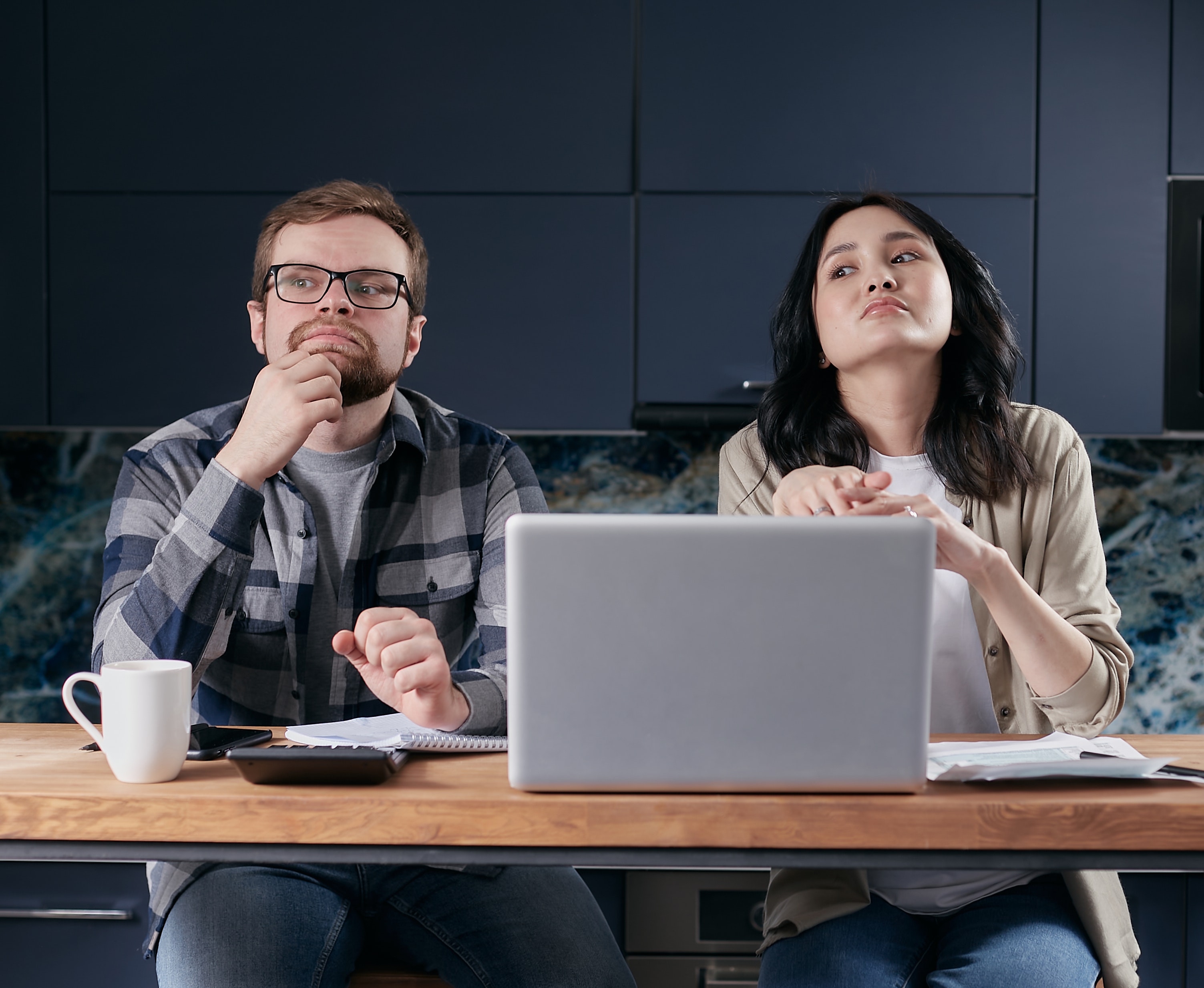 A couple looking bored and evasive, sitting in front of a computer and calculator.