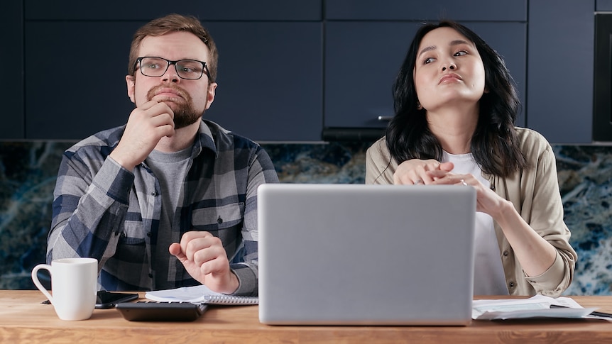 A couple looking bored and evasive, sitting in front of a computer and calculator.