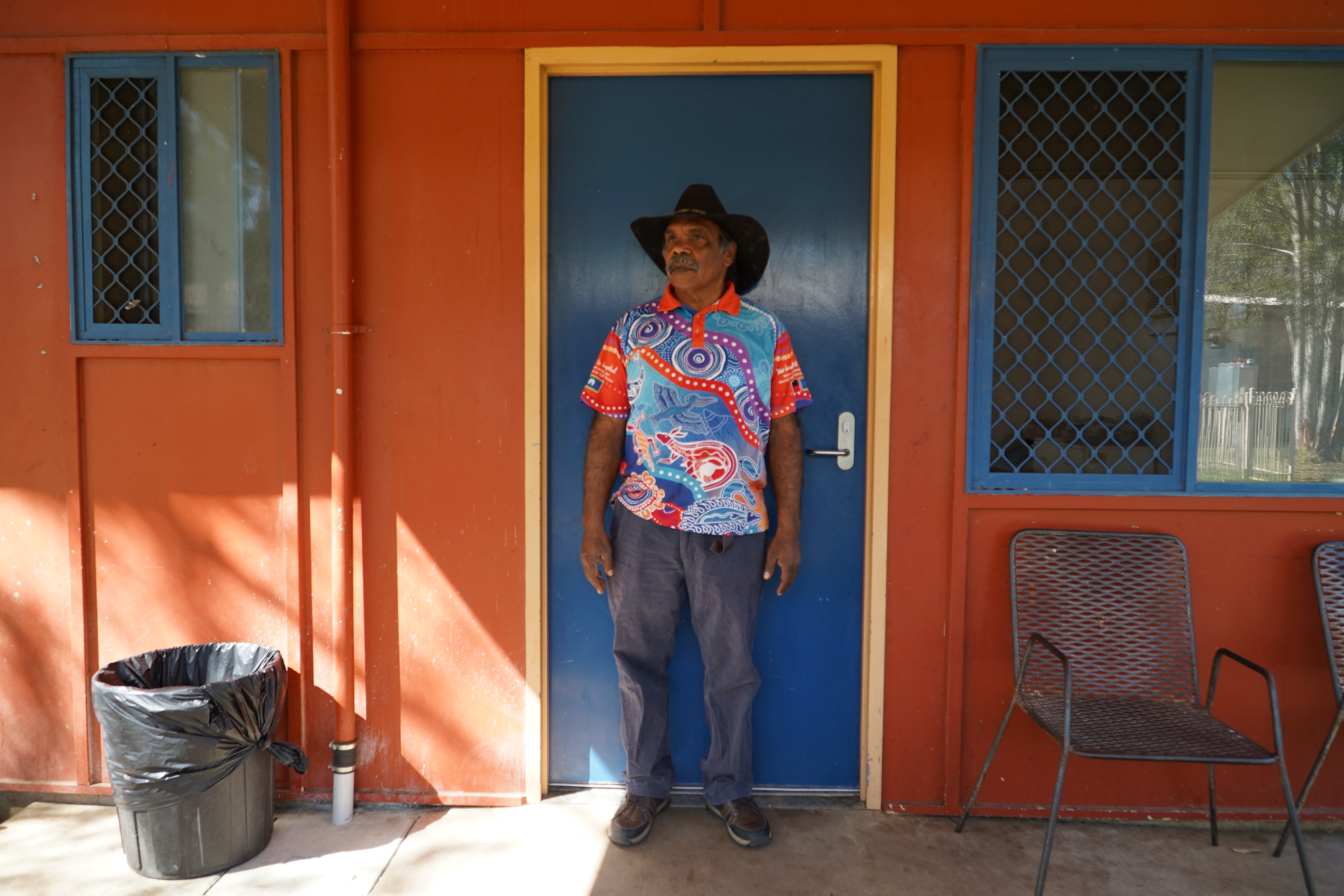 Tim McNamara, an Indigenous man wearing a black cowboy hat and colourful shirt, stands in front of a door.