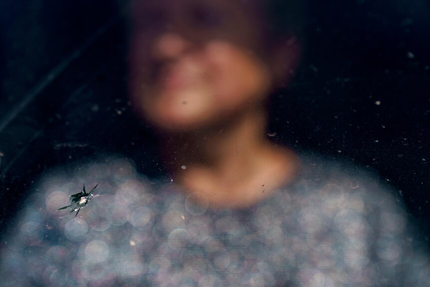 An in focus crack in a windshield with a woman out of focus in the background