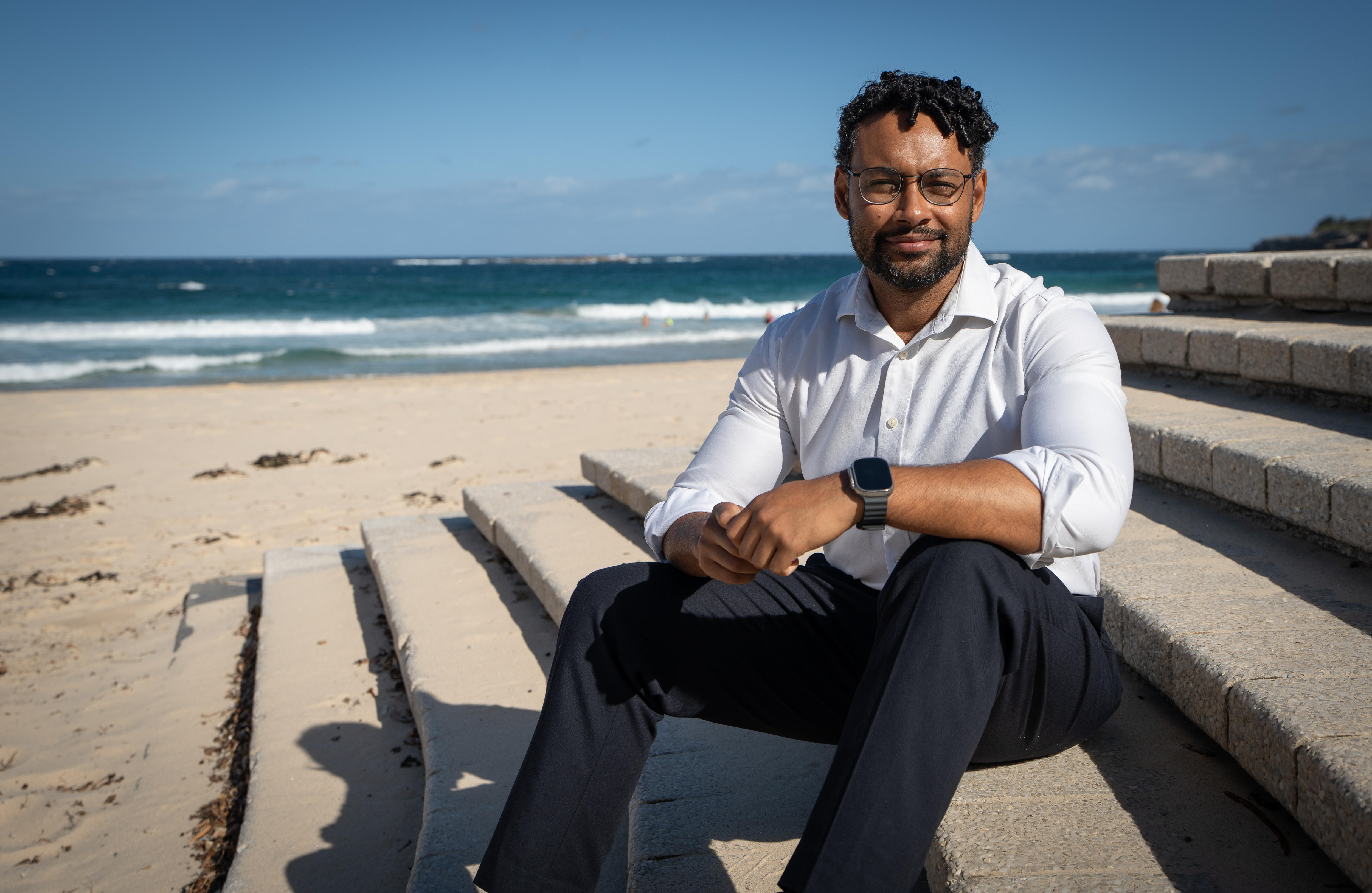 Um homem está sentado nos degraus que levam à areia de uma praia.