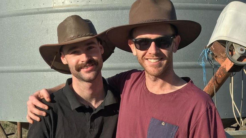 Two smiling men with moustaches, wearing broad-brimmed hats, with their arms around each other.