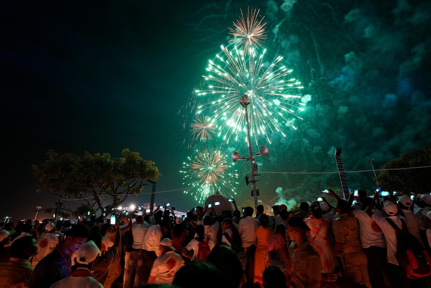 Green fireworks light up the sky over a crowd of people. 