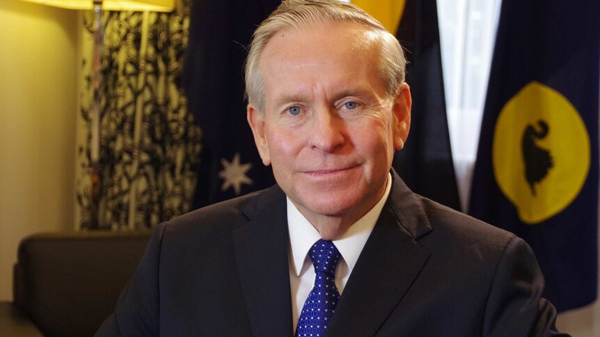 Western Australia's Premier Colin Barnett pose for a picture with a WA flag in the background ahead of a TV interview.