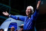 Wally Funk stands on stage smiling with arms open in celebration after completing space mission. 