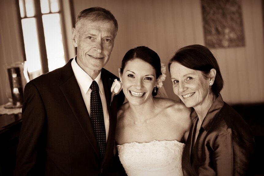 Jill and Roger in suit and formal dress, with their daughter on her wedding day