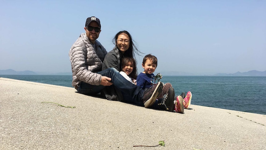 A father, mother, daughter and son sitting on a concrete platform by the sea.