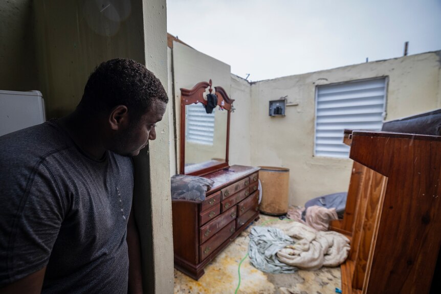 A man looks into a room of his house with the roof missing.