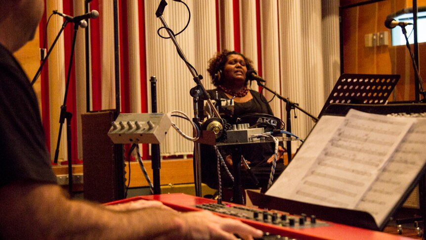 A woman sings in a studio while a man plays keyboard.