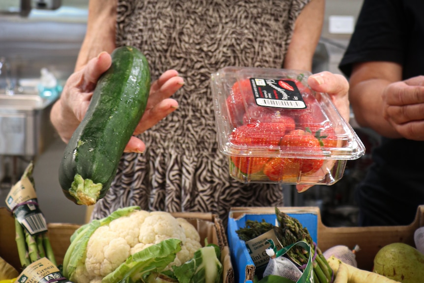 A woman holding a zucchini and strawberries