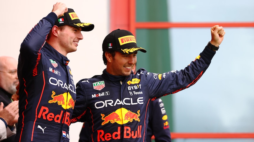Two F1 drivers raise thier fists in celebration on the podium.