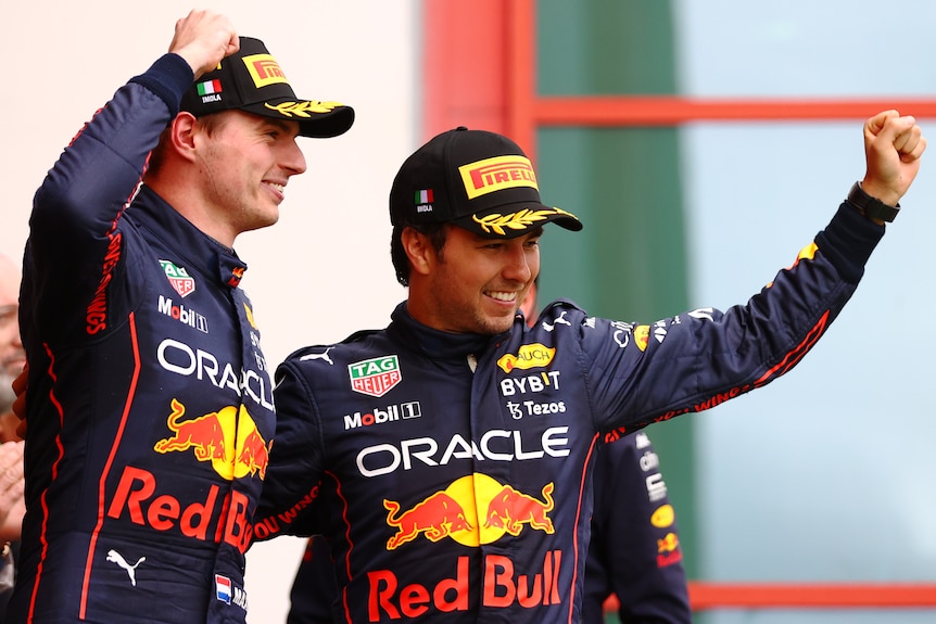 Two F1 drivers raise thier fists in celebration on the podium.