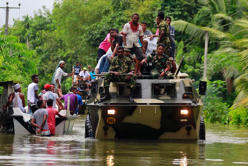 Sri Lankan soldiers drive large military vehicles through floodwaters to evacuate victims, a boat of people paddles next to one.
