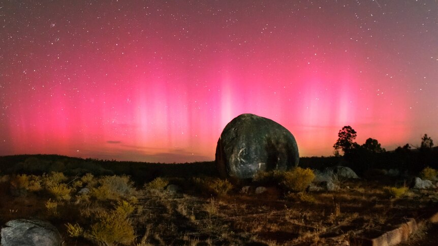 A glowing pink sky with a boulder in the foreground.