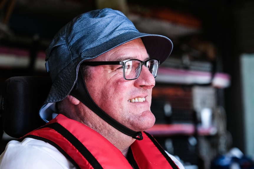 A close up portrait of a man wearing black glasses and a blue brimmed bucket hat, profile view.