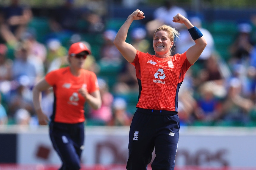 Katherine Brunt stands, smiling, with both arms in the air after taking a wicket