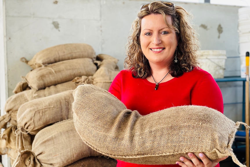 A woman smiles at the camera while holding hessian sacks filled with coffee.