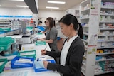 Three pharmacist lined up behind the counter preparing scripts, printing labels and writing out medications.