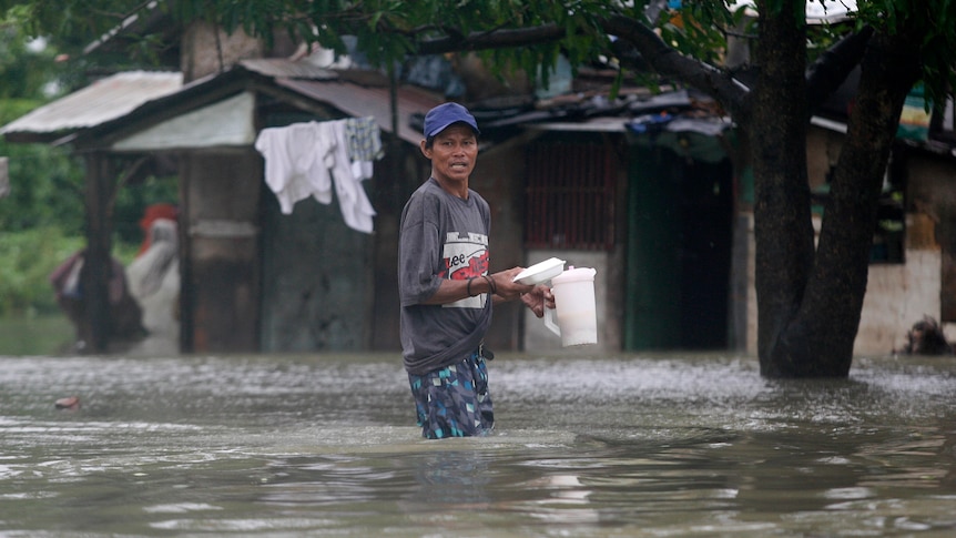 A resident carries food as he returns to his submerged house