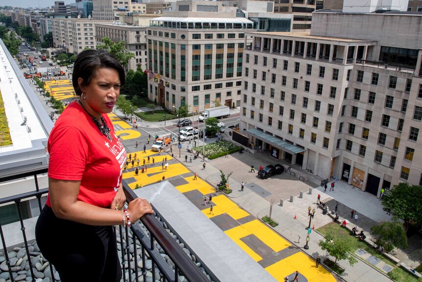Muriel Bowser stands on a rooftop looking out at a massive Black Lives Matter street mural painted in bright yellow