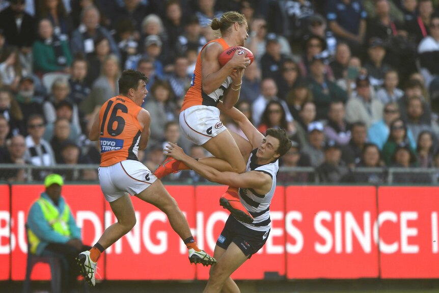 An AFL player leaps highest to take a mark ahead of an opponent