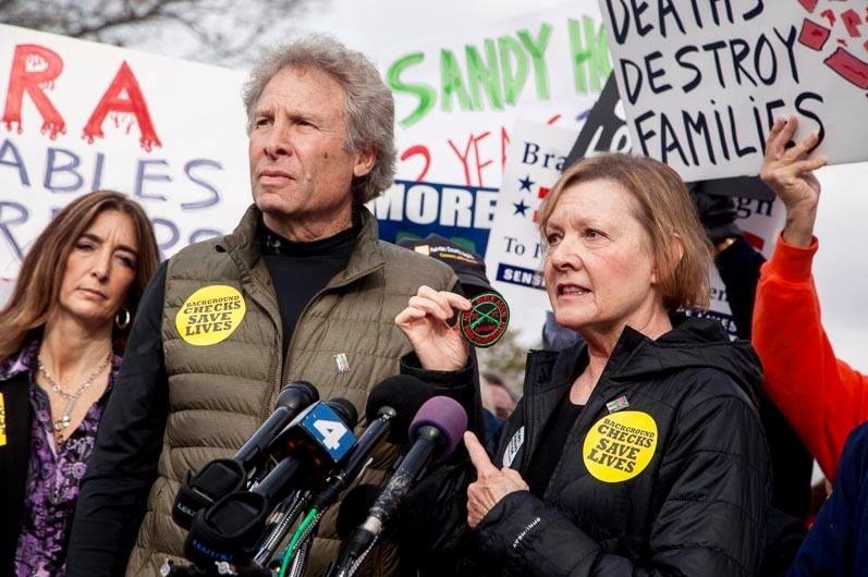 A man and a woman at a protest wearing 'Checks Save Lives' stickers on their jackets