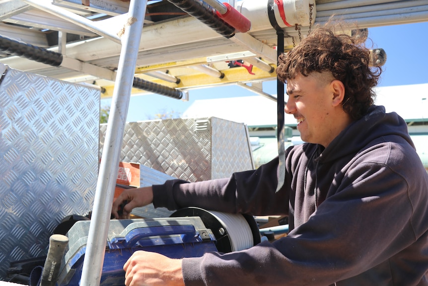 A man opens a tool box on the back of a ute.