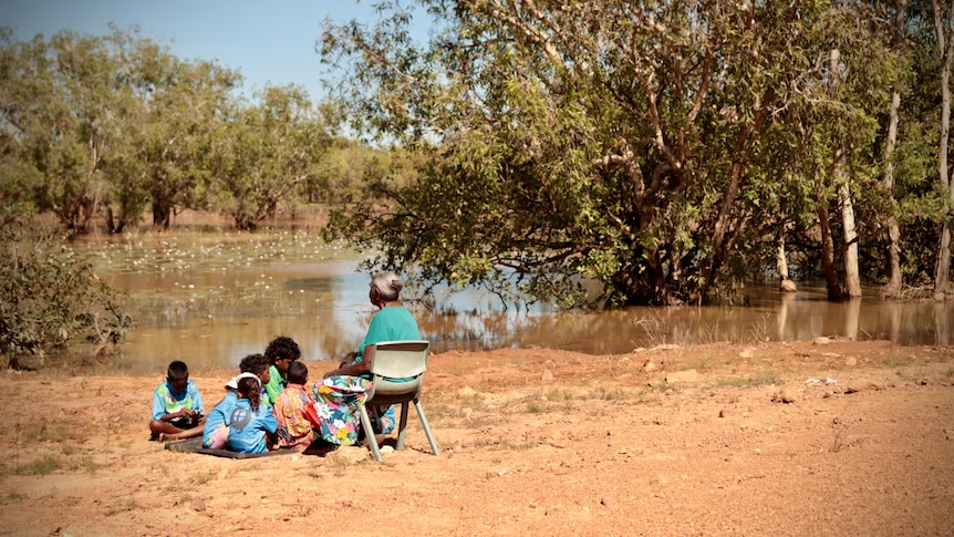 Miriam-Rose Ungunmerr Baumann teaches the kids about lillies as they sit next to a creek