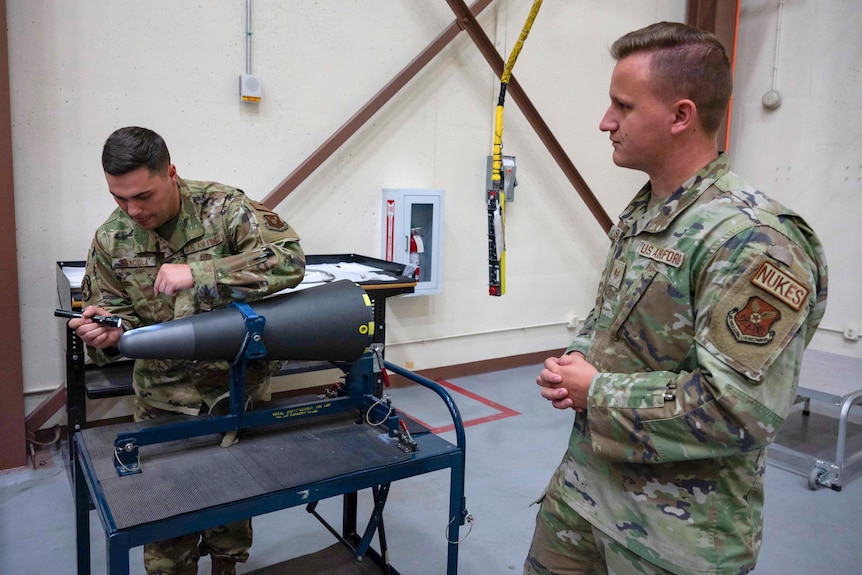 A US airmen in uniform works on a nuclear warhead as another stands nearby