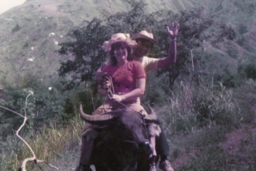 An old photo of a couple sitting on a buffalo in a mountainous area.