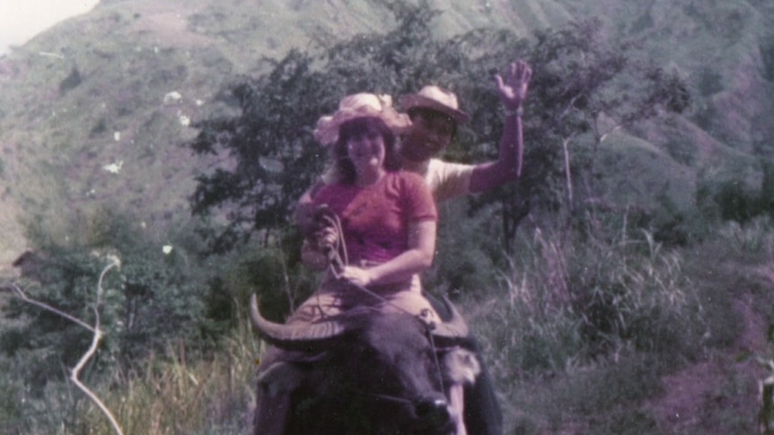 An old photo of a couple sitting on a buffalo in a mountainous area.