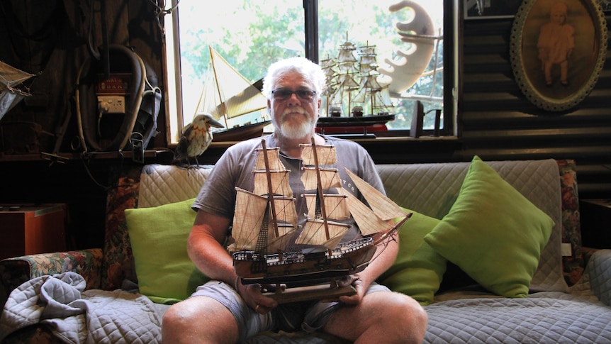 Kevin sits on a couch holding a model tall ship.