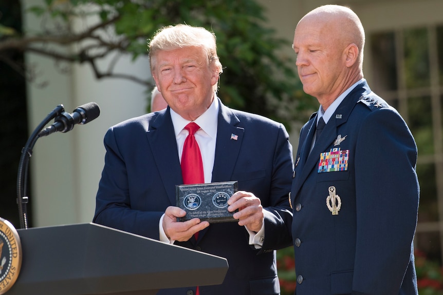 Former US president Donald Trump smiles as he receives a plaque from a man in army uniform.