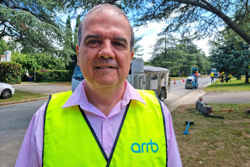 Michael smiles near roadworks, wearing a high-vis bib.