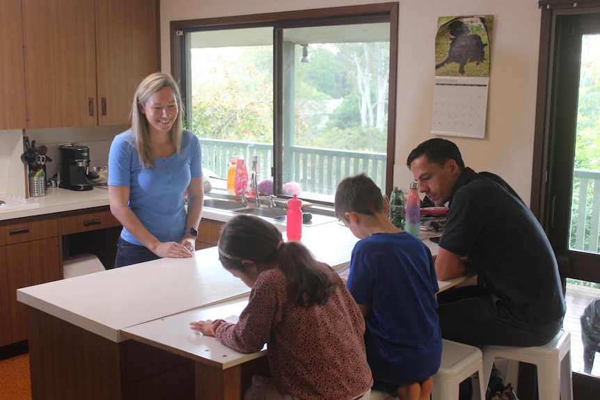 A woman and her husband watch as the kids do homework.