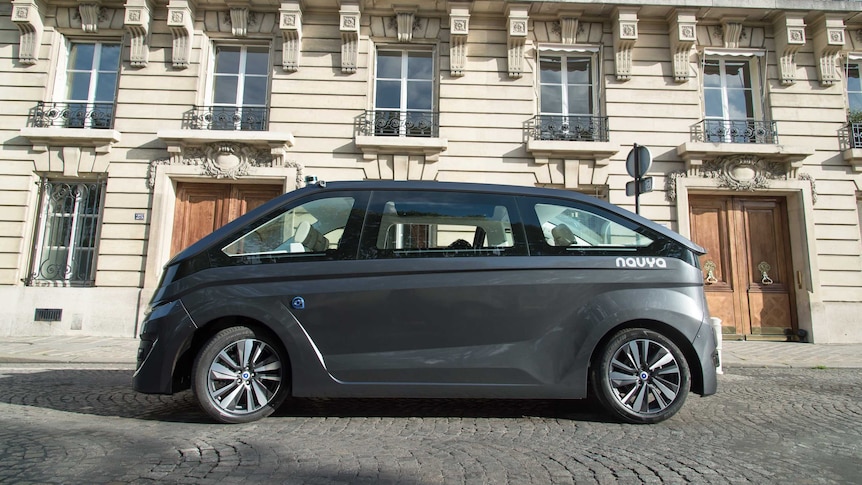 A black NAVYA driverless car sits parked on the side of a Paris road.