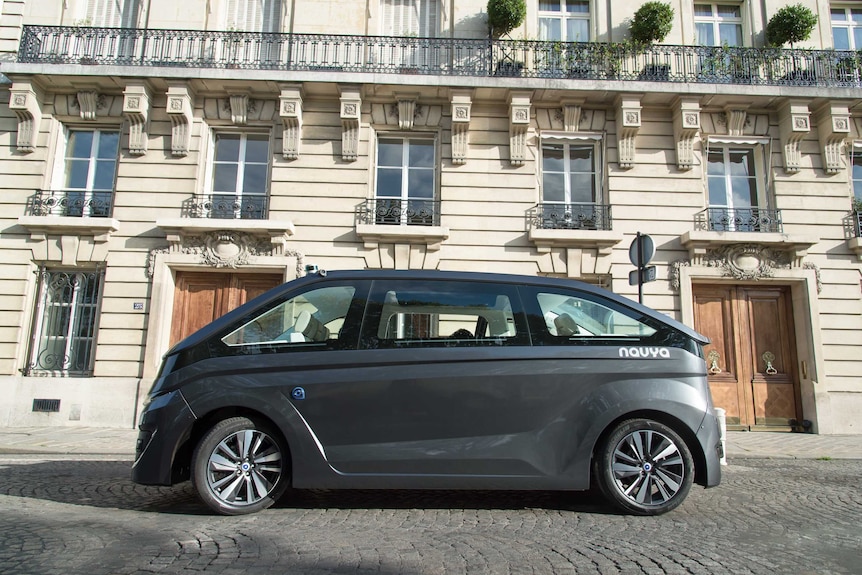 A black NAVYA driverless car sits parked on the side of a Paris road.