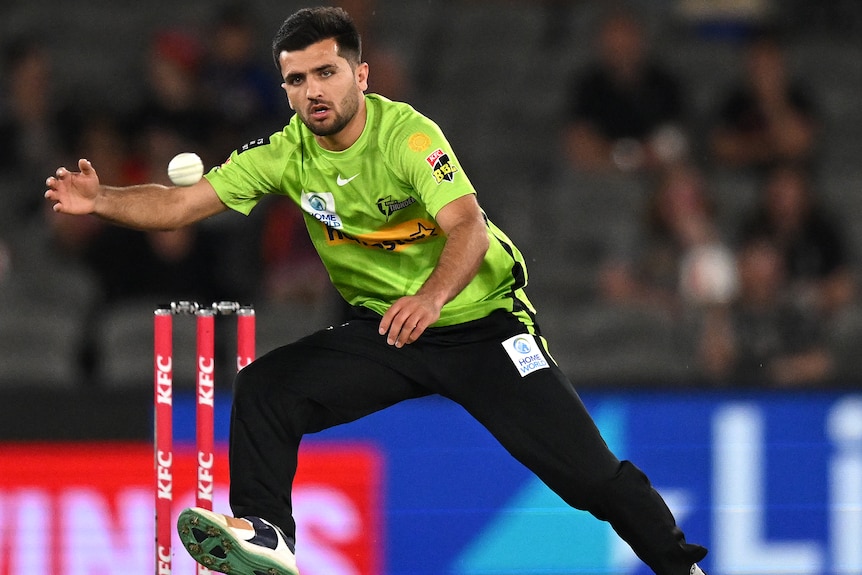 A Sydney Thunder BBL player stretches out his right hand as he tries to  field a ball during a match.