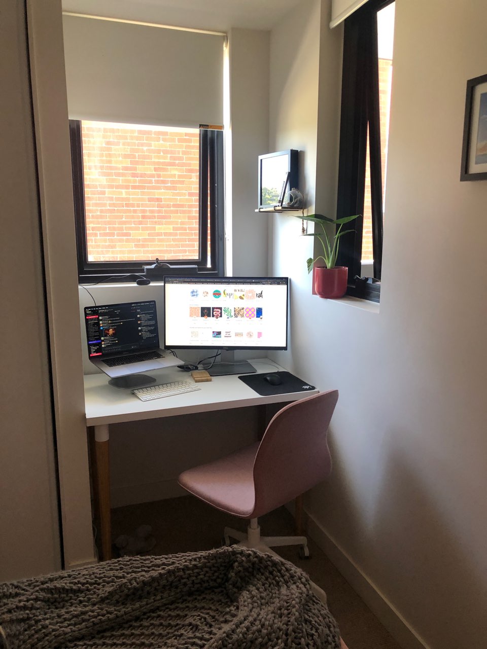 A small desk set up in front of a window looking out onto a brick wall.