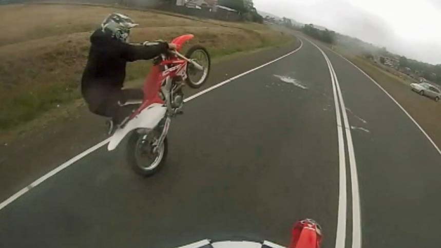 A motorcyclist rides on one wheel on a Tasmanian road on an online video.