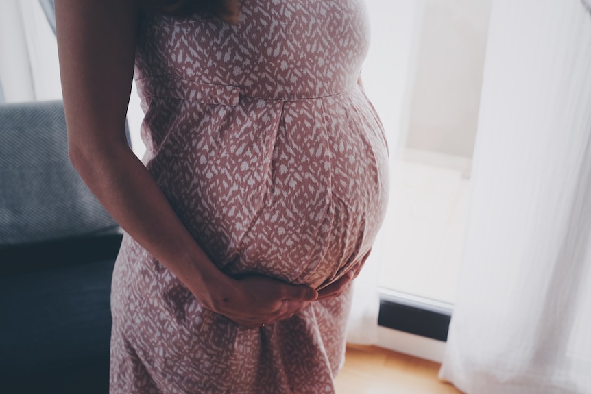 A close up photo of a woman in a printed dress, her hands on her pregnant belly